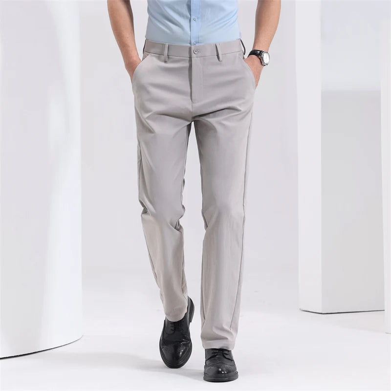 Man wearing light gray slim-fit cotton dress trousers with black oxford shoes and light blue shirt, hands in pockets.