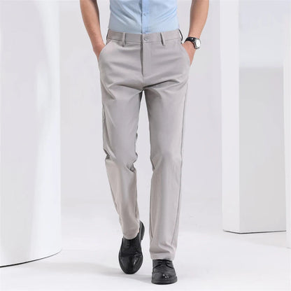 Man wearing light gray slim-fit cotton dress trousers with black oxford shoes and light blue shirt, hands in pockets.