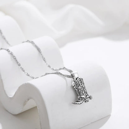 Silver necklace with intricate filigree cowboy boot charm pendant displayed on white ceramic jewelry stand