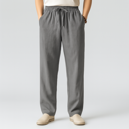 Men's gray linen drawstring pants with elastic waist, side pockets, straight leg fit, paired with beige slip-on shoes.