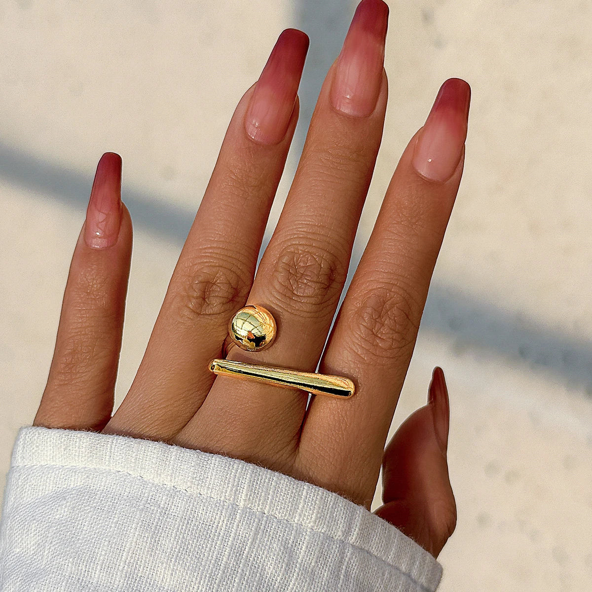 Gold-tone adjustable open bar and ball ring on woman's hand with red ombre manicure nails