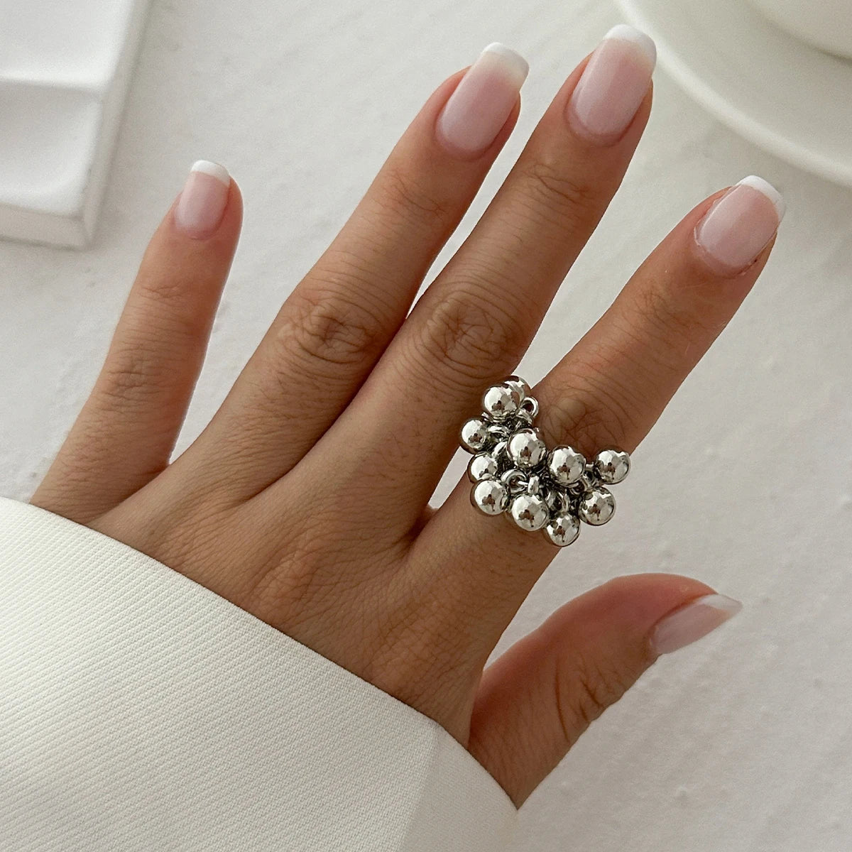 Silver adjustable beaded cluster ring worn on middle finger, shown with French manicured nails on white background.