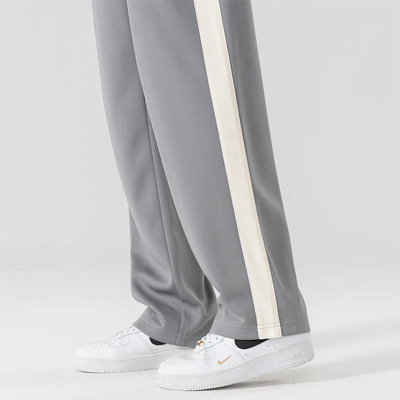 Gray wide-leg men's sweatpants with cream side stripe, worn with white Nike Air Force 1 sneakers, side view.