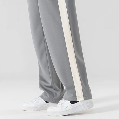Gray wide-leg men's sweatpants with cream side stripe, worn with white Nike Air Force 1 sneakers, side view.