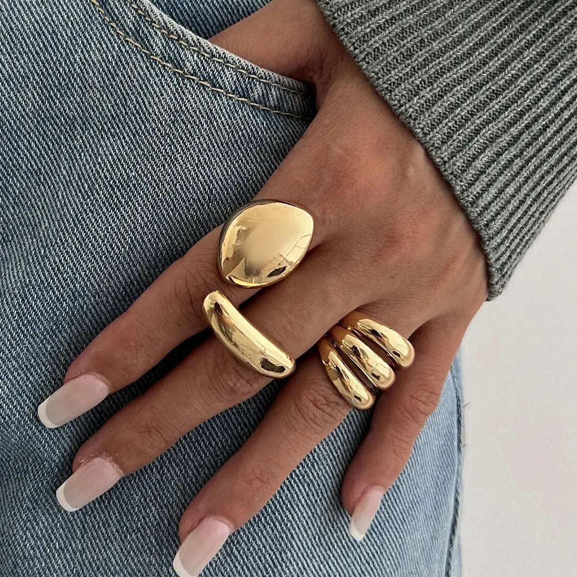 Gold chunky adjustable statement rings set on woman's hand with denim jeans background modern minimalist jewelry