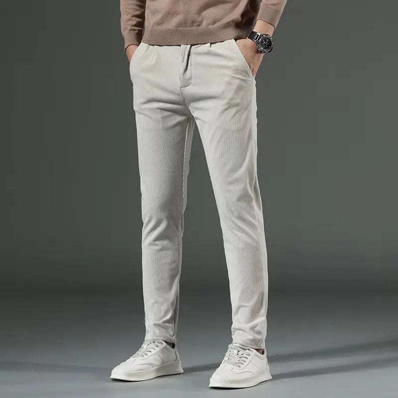 Men's slim fit cream corduroy chino pants with elastic waist, paired with white sneakers and beige sweater