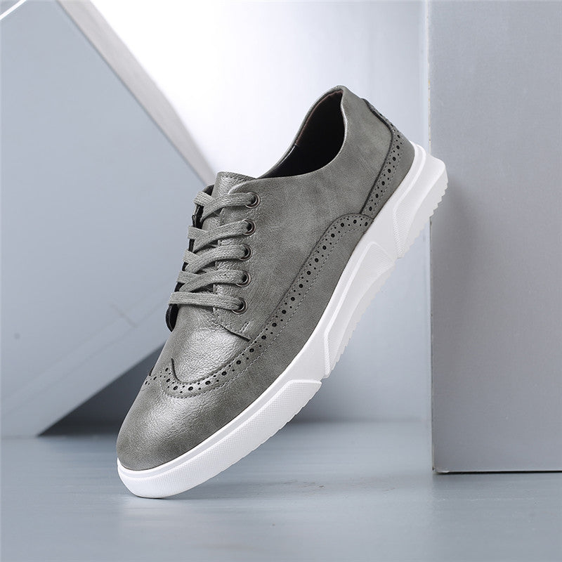 Gray men's brogan leather lace-up sneakers with brogue detailing and white rubber sole on neutral background