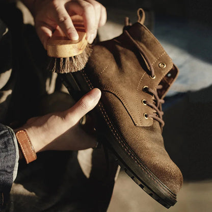 Man brushing brown suede lace-up ankle boots with a horsehair brush for cleaning and maintenance.