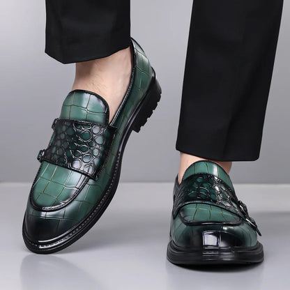 Green croc-embossed leather double monk strap loafers worn with black dress trousers, shown from ankle down.