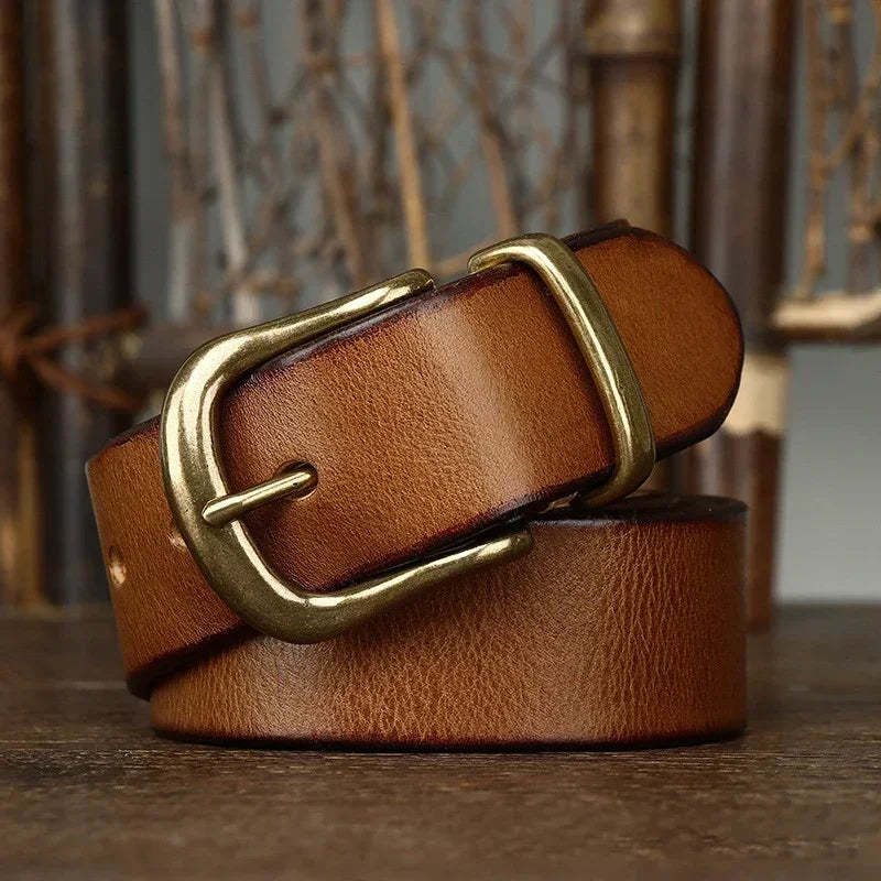 Brown genuine leather men's belt with antique brass pin buckle, coiled on rustic wooden surface