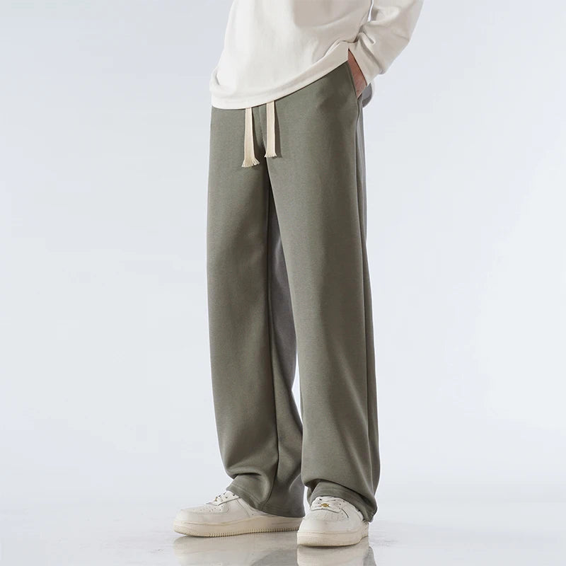Men's olive green cotton wide-leg relaxed-fit pants with drawstring waist and cream sneakers