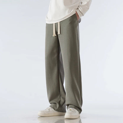 Men's olive green cotton wide-leg relaxed-fit pants with drawstring waist and cream sneakers