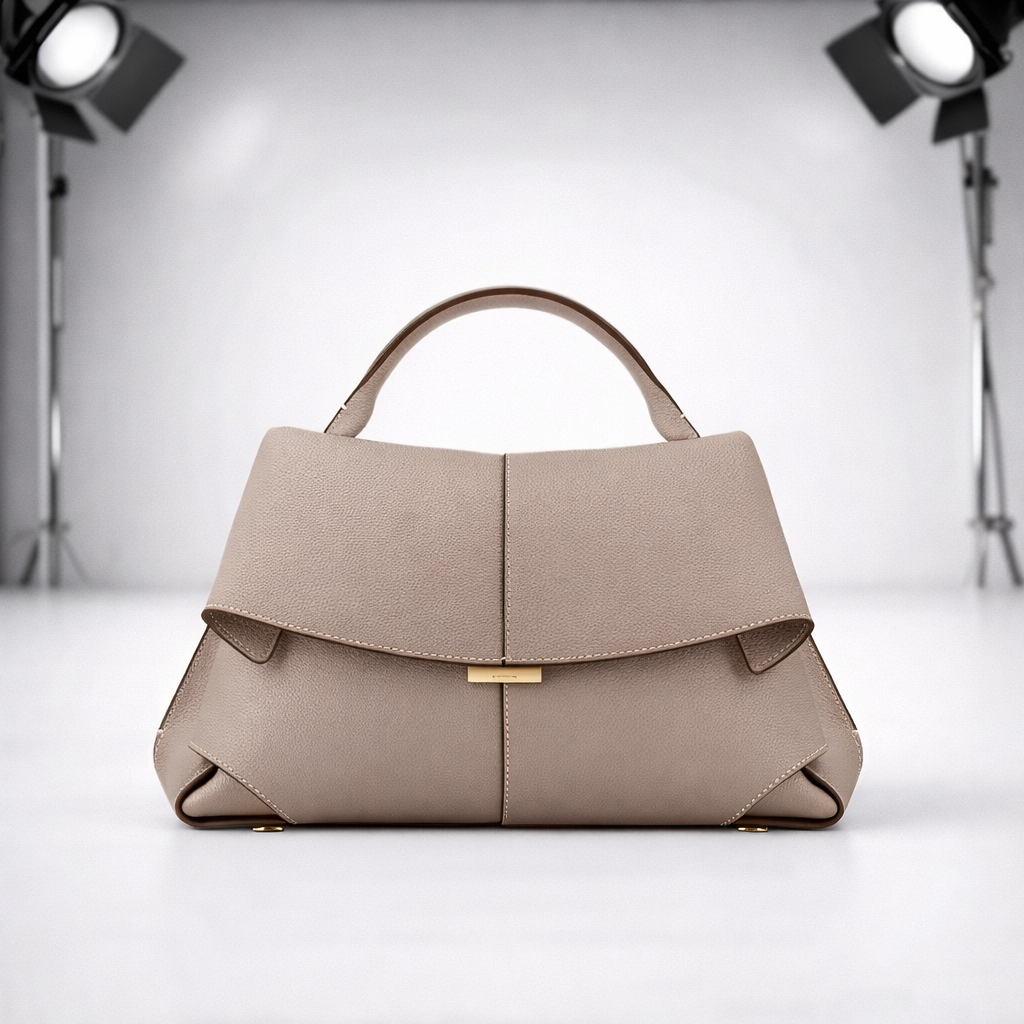 Structured taupe pebbled leather women's handbag with top handle, flap closure, gold hardware, and origami-folded corners.