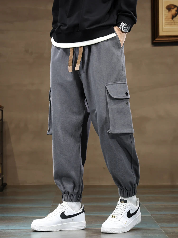 Gray men's cargo jogger pants with side pockets, drawstring waist, tapered fit, paired with white Nike sneakers.