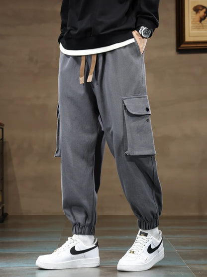 Gray men's cargo jogger pants with side pockets, drawstring waist, tapered fit, paired with white Nike sneakers.