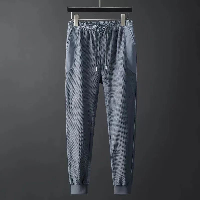 Men's blue-gray jogger pants with mesh texture, elastic waistband, drawstring, side pockets, and ribbed cuffs