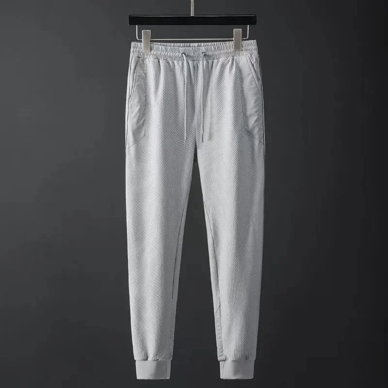 Light gray men's jogger pants with textured mesh fabric, elastic waistband, drawstring, side pockets, and ribbed cuffs