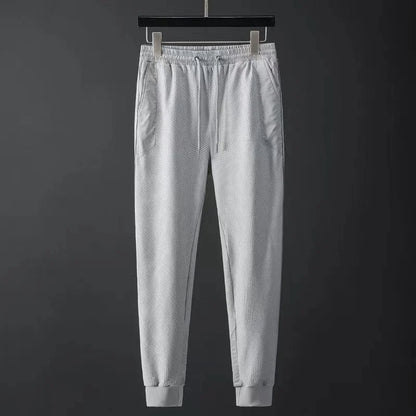 Light gray men's jogger pants with textured mesh fabric, elastic waistband, drawstring, side pockets, and ribbed cuffs