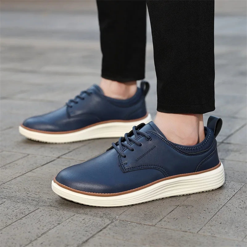 Navy blue men's leather lace-up casual shoes with white platform sole, worn with black pants on cobblestone surface.