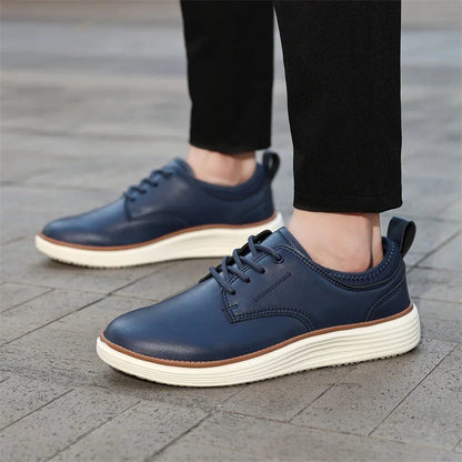Navy blue men's leather lace-up casual shoes with white platform sole, worn with black pants on cobblestone surface.