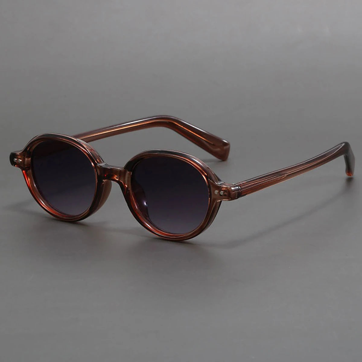 Round sunglasses with transparent brown frames, dark gradient lenses, and slim tortoiseshell temples on gray background