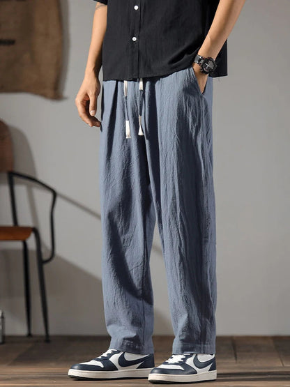 Men's wide-leg blue linen drawstring pants styled with black shirt and navy sneakers, relaxed fit with tassel tie waist