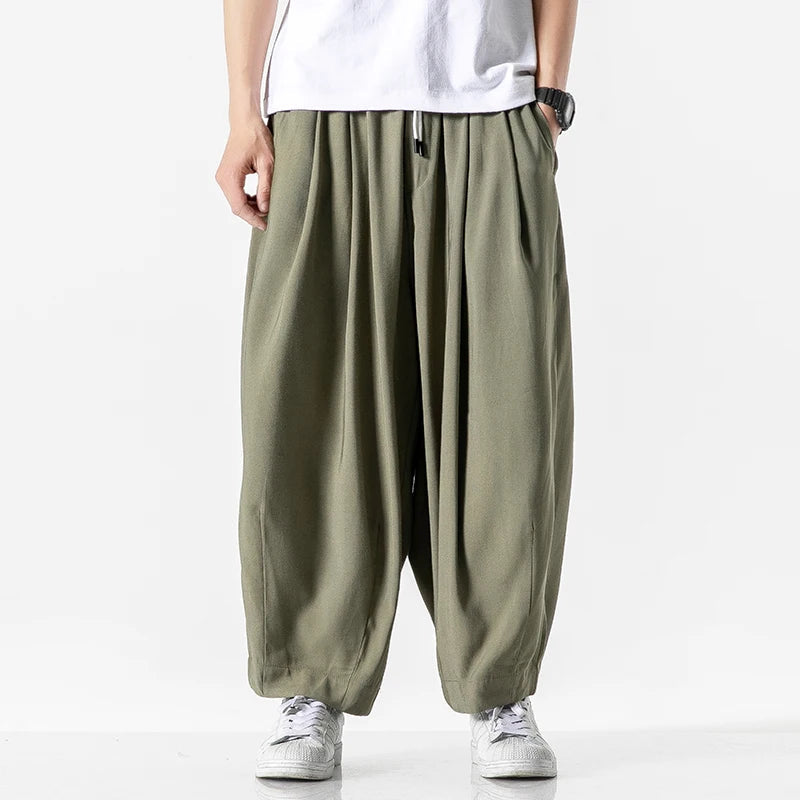 Men's wide-leg olive green cotton drawstring harem pants with elastic waist, paired with white tee and sneakers.