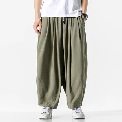 Men's wide-leg olive green cotton drawstring harem pants with elastic waist, paired with white tee and sneakers.
