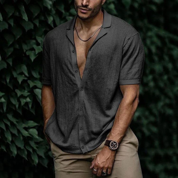 Man wearing dark gray short sleeve button-down linen shirt with khaki pants and brown leather watch outdoors.