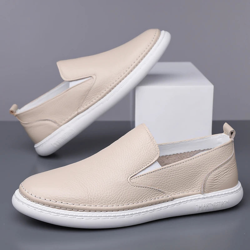 Beige leather slip-on loafers for men with white rubber sole, minimalist design, and elastic side panels.