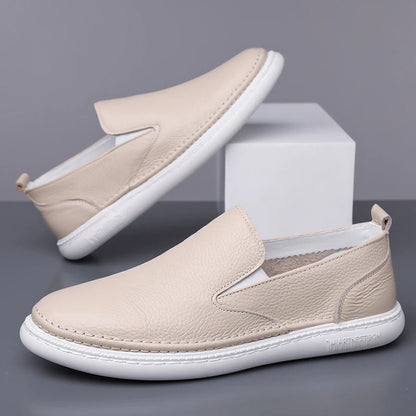 Beige leather slip-on loafers for men with white rubber sole, minimalist design, and elastic side panels.