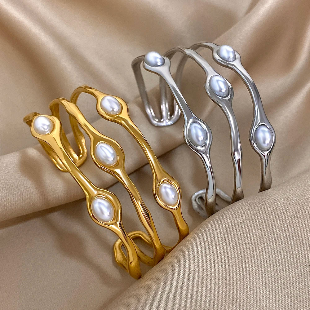 Gold and silver open cuff bangles with embedded white oval pearls displayed on beige satin fabric