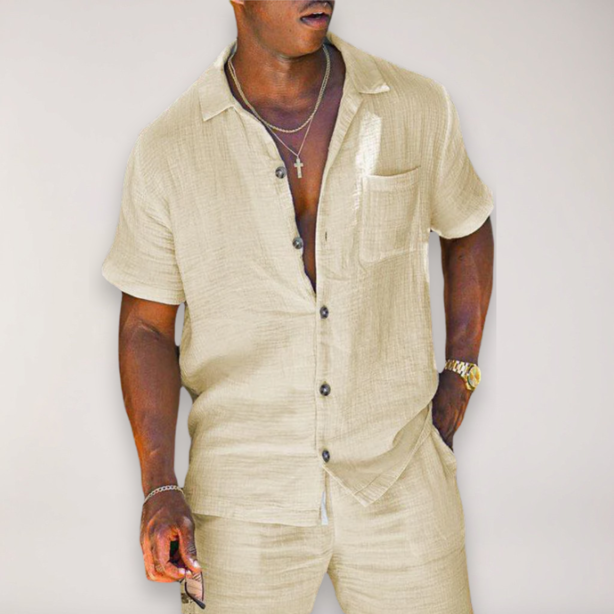 Man wearing beige short-sleeve linen button-up shirt and matching pants, styled with gold jewelry and watch.