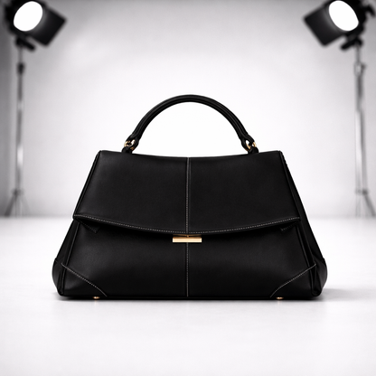 Black structured leather top handle handbag with gold clasp closure, white contrast stitching, and gold-tone feet on white background.