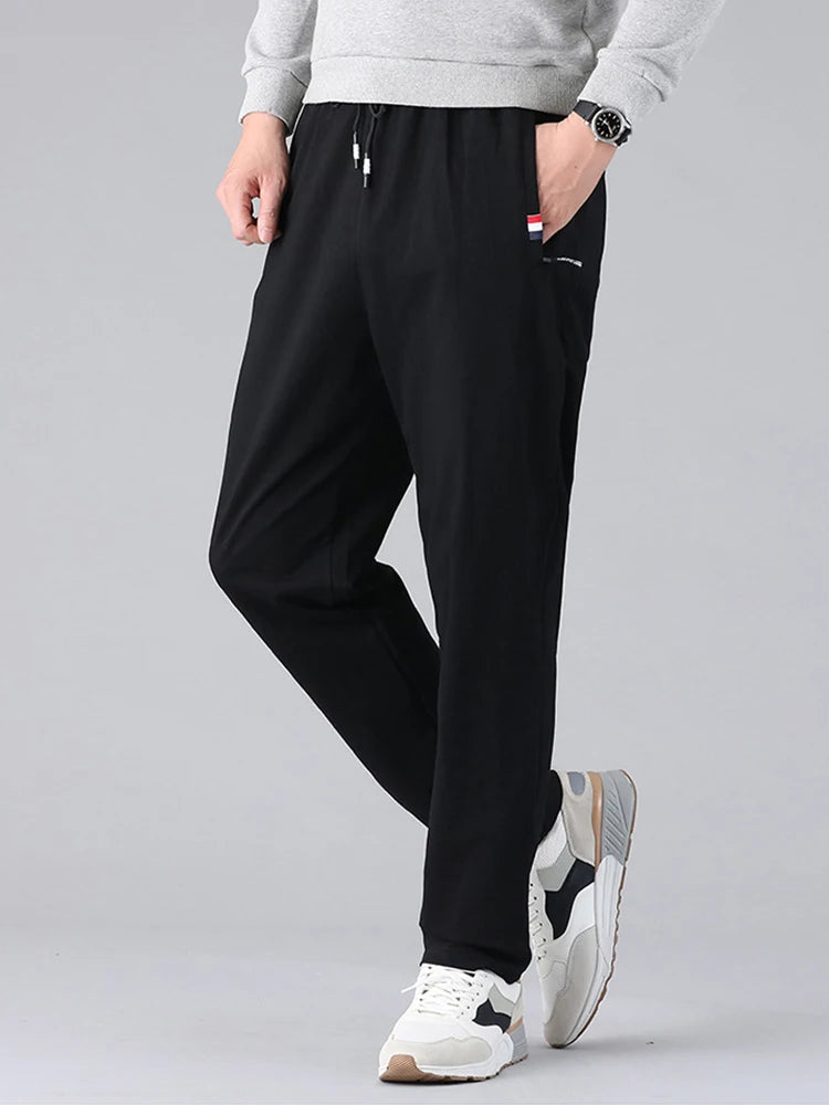 Men's black cotton drawstring sweatpants with side pockets, worn with gray sweatshirt and white sneakers