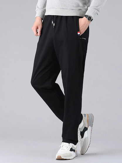 Men's black cotton drawstring sweatpants with side pockets, worn with gray sweatshirt and white sneakers