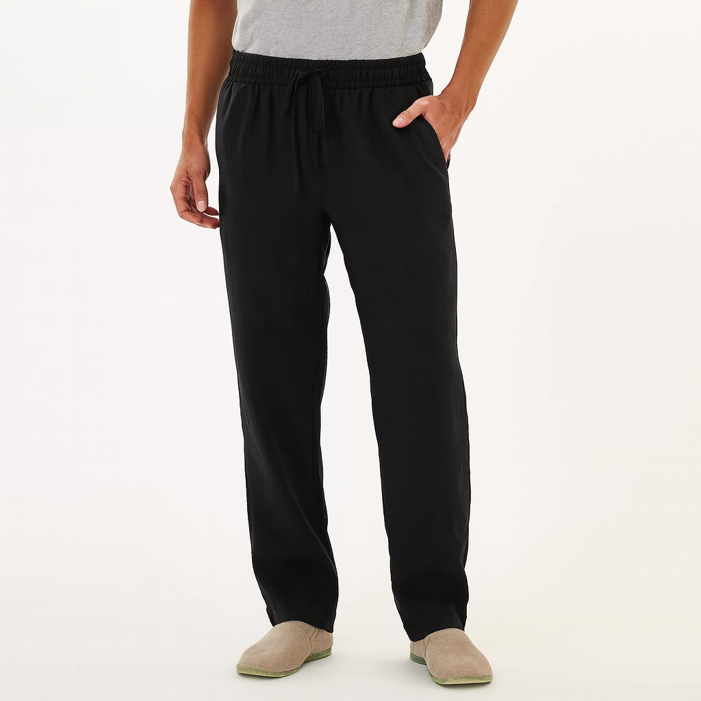 Man wearing black cotton drawstring pants with elastic waist, side pockets, and relaxed fit, paired with beige slip-on shoes.