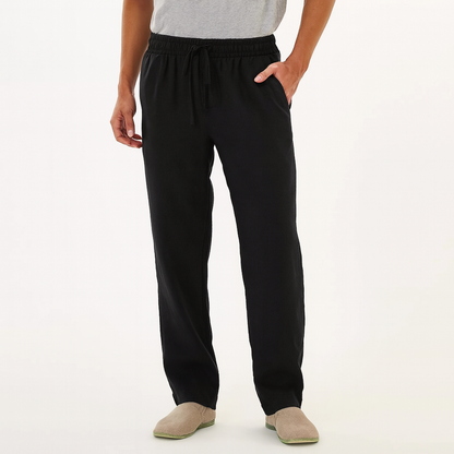Man wearing black cotton drawstring pants with elastic waist, side pockets, and relaxed fit, paired with beige slip-on shoes.