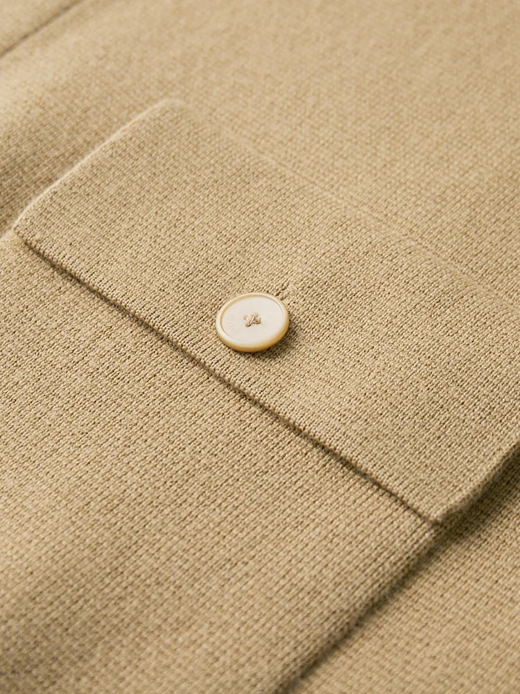 Close-up of a tan merino wool cardigan jacket cuff featuring a cream mother-of-pearl button on a knit flap pocket.
