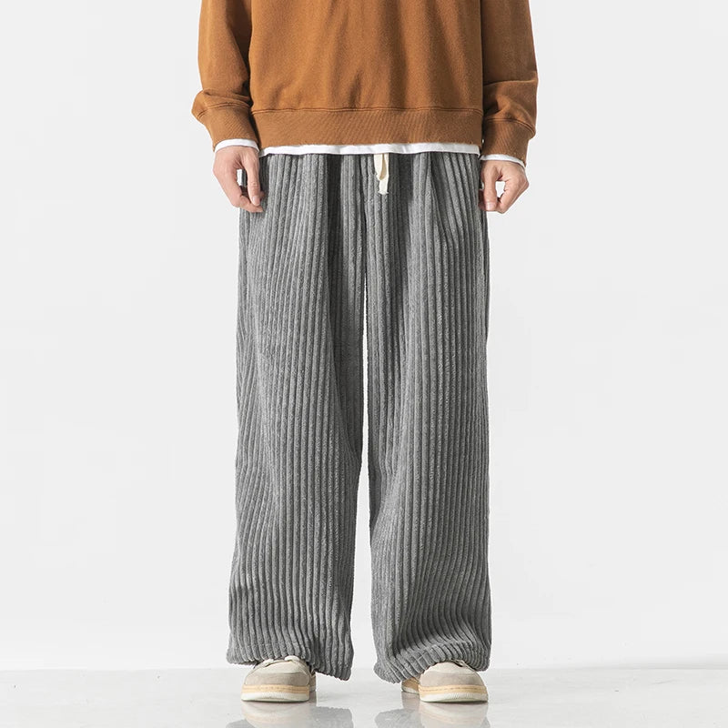Gray wide-leg corduroy drawstring pants paired with a rust brown sweatshirt and white sneakers on male model