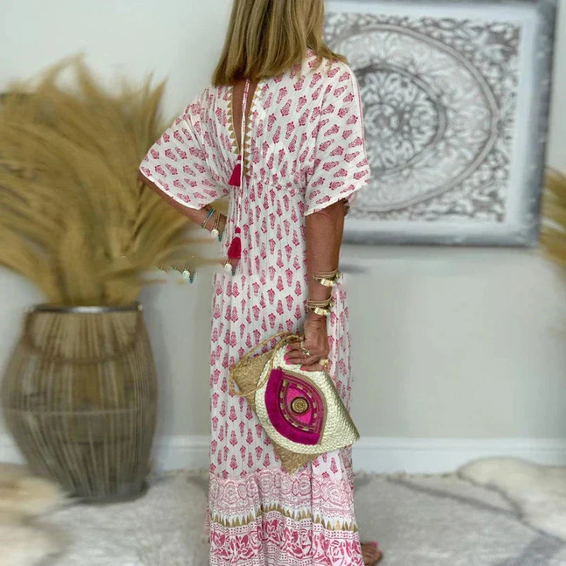 Woman wearing white and pink boho printed maxi dress with short sleeves, holding a woven pink clutch bag.