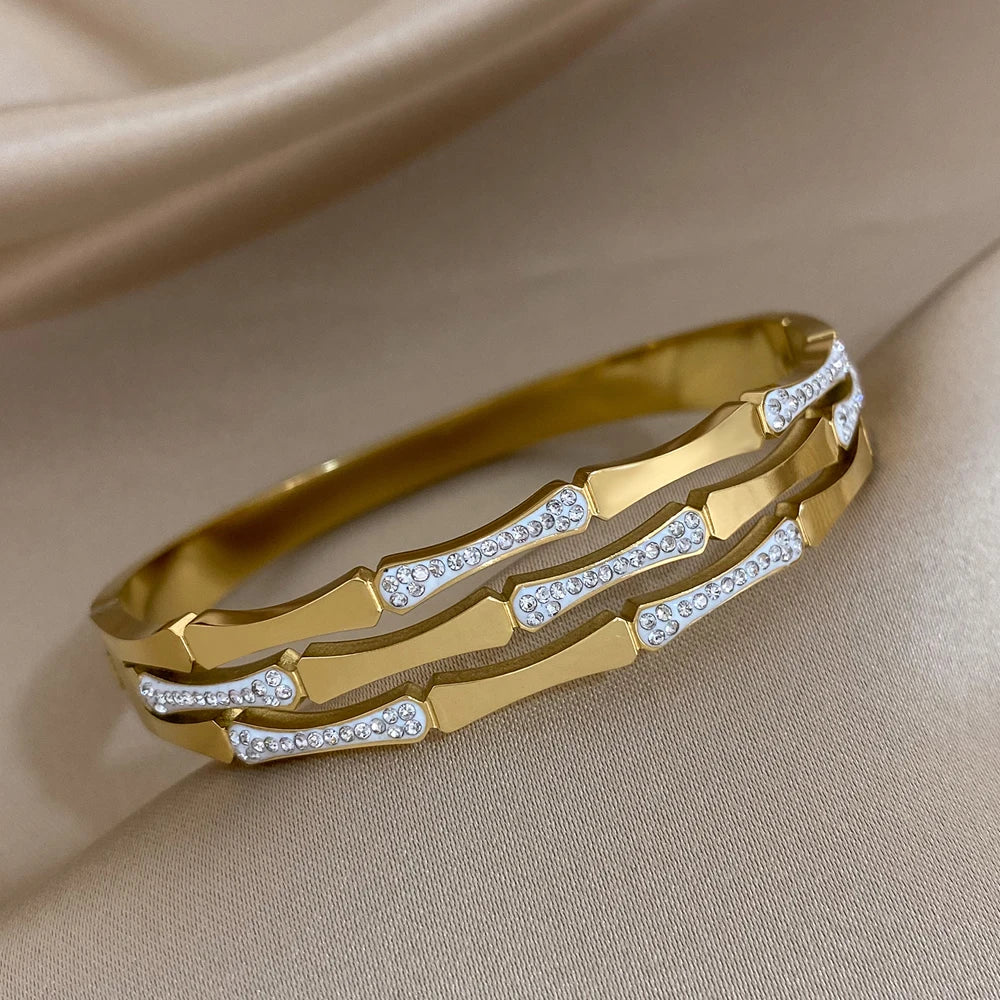 Gold tone geometric bangle bracelet with sparkling crystal stone accents on satin fabric background