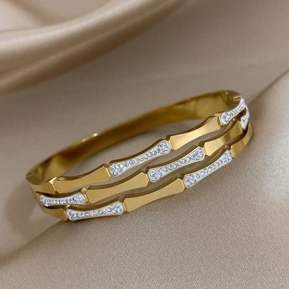Gold tone geometric bangle bracelet with sparkling crystal stone accents on satin fabric background