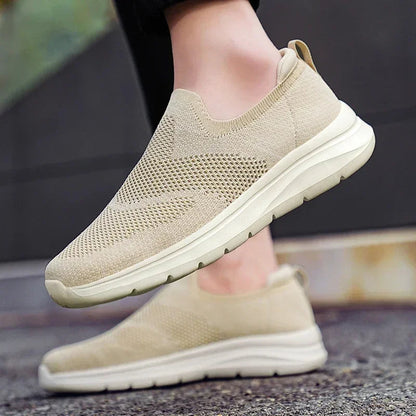 Beige women's slip-on mesh knit sneakers with white sole, shown from side angle on model's feet.
