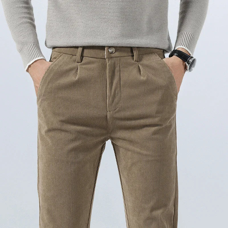 Men's khaki corduroy slim fit pants with pleated front, side pockets, paired with a light gray knit sweater.