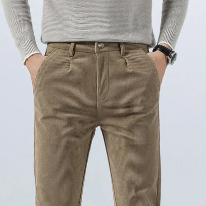 Men's khaki corduroy slim fit pants with pleated front, side pockets, paired with a light gray knit sweater.