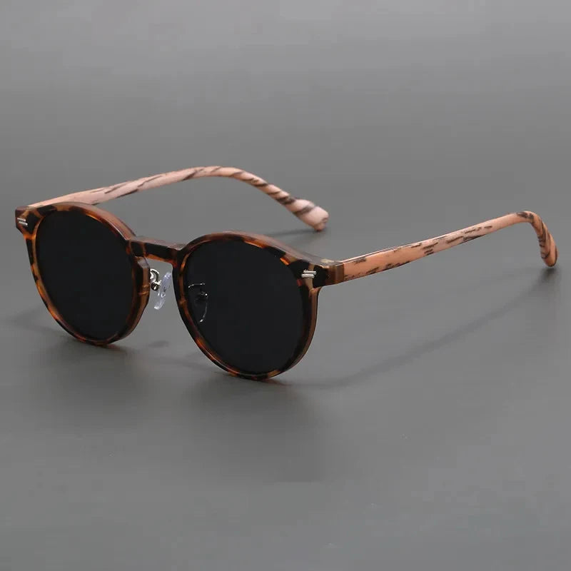 Round tortoiseshell sunglasses with dark black lenses and striped brown frame on gray background