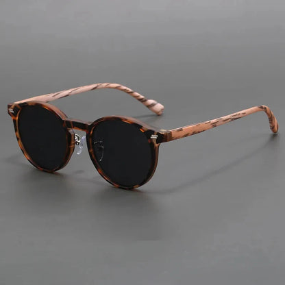 Round tortoiseshell sunglasses with dark black lenses and striped brown frame on gray background