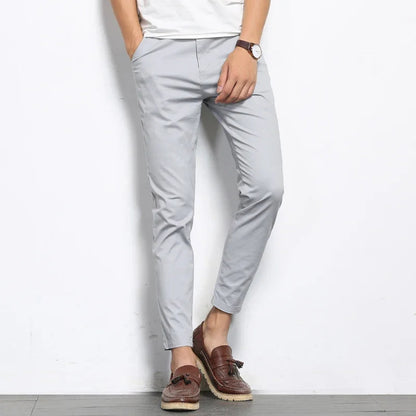 Men's light gray slim fit cotton chino pants paired with brown tassel loafers and white tee, cropped ankle length.