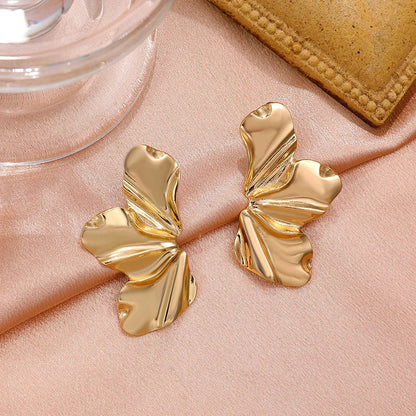 Gold tone ruffled statement earrings with textured petal design displayed on pink satin fabric